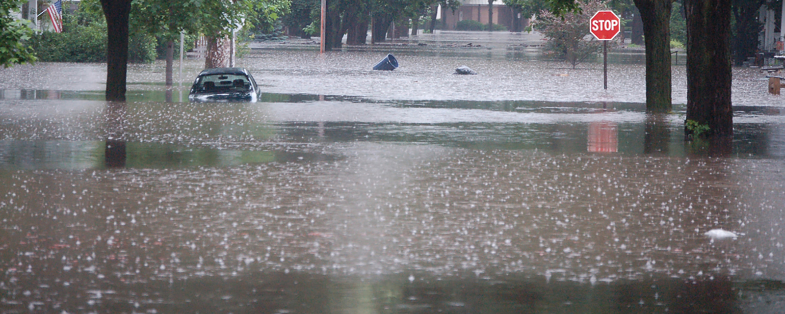 A flooded street with a half-submerged car and a stop sign